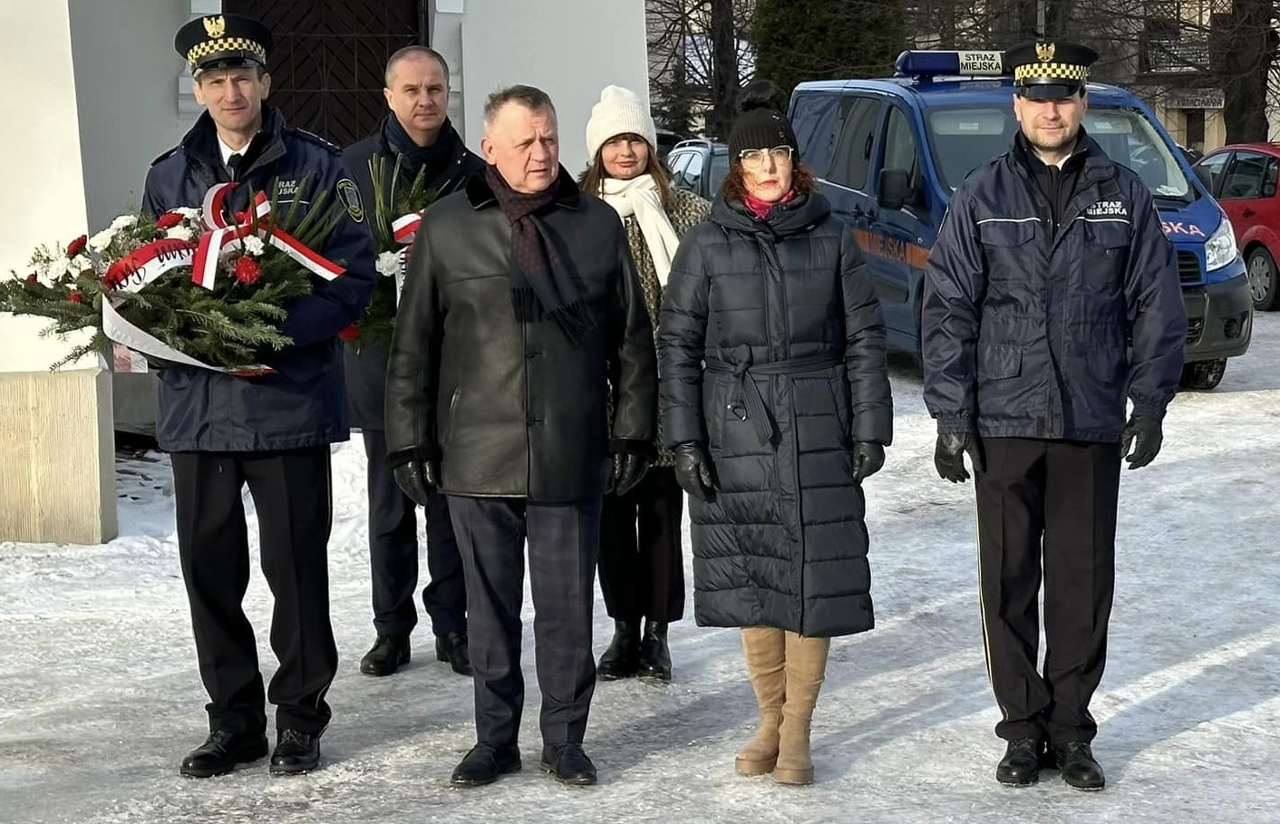 Grupa ludzi składa wiązanke przed pomnikiem. 